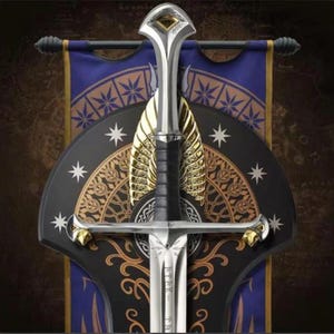May include: A silver-toned sword with a black grip and gold-coloured accents on the pommel and crossguard. The blade features engraved runic characters. It is mounted against a dark blue and black shield-shaped plaque with gold star motifs.