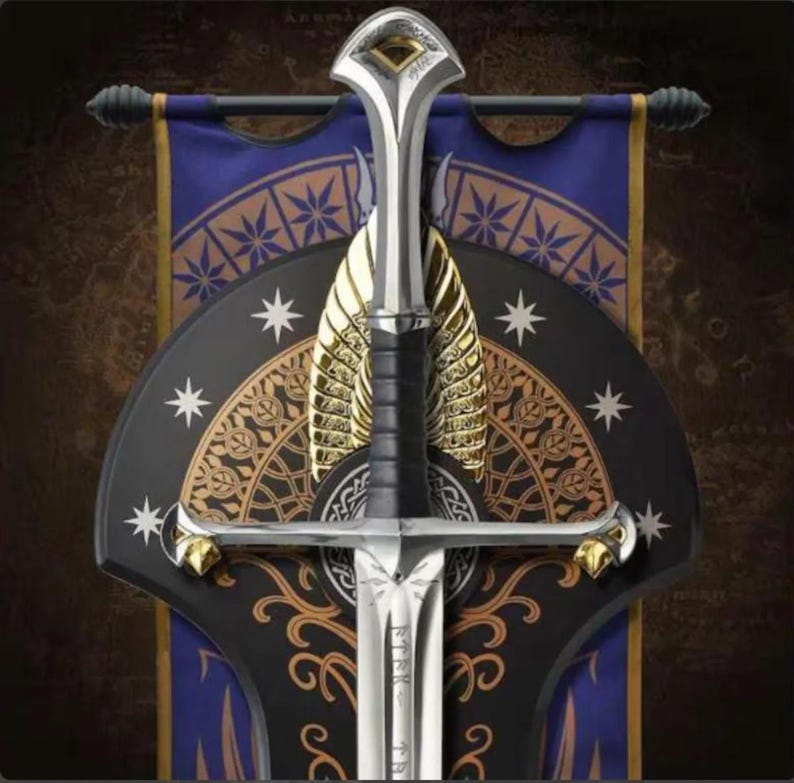 May include: A silver-toned sword with a black grip and gold-coloured accents on the pommel and crossguard. The blade features engraved runic characters. It is mounted against a dark blue and black shield-shaped plaque with gold star motifs.