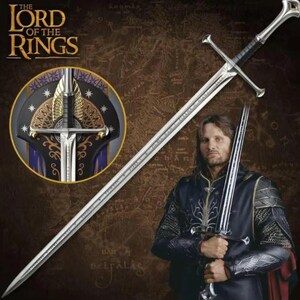 May include: A silver metal longsword with a crossguard and a black grip, featuring an intricate pommel. The blade is long and pointed. A circular inset shows a detailed view of the sword hilt with gold-coloured wing-like accents.