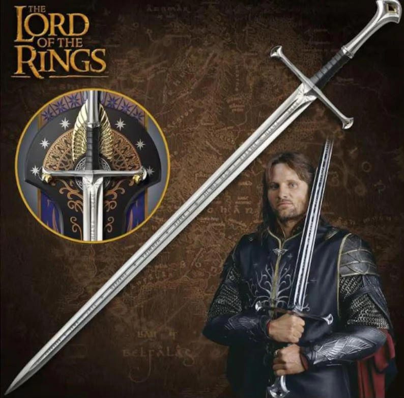 May include: A silver metal longsword with a crossguard and a black grip, featuring an intricate pommel. The blade is long and pointed. A circular inset shows a detailed view of the sword hilt with gold-coloured wing-like accents.