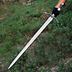 May include: A long, double-edged steel sword with a pointed tip and a central fuller running down the blade. The hilt features a curved crossguard with intricate silver-toned detailing and a black grip, held by a gloved hand against greenery.