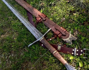 May include: A long sword with a patterned metal blade, a wooden handle featuring intricate carvings, and a metal pommel. It is accompanied by a matching brown leather scabbard with embossed designs and a leather belt with metal hardware.