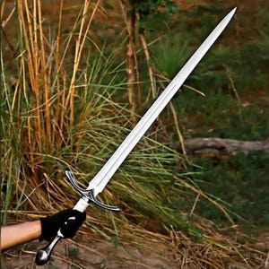 May include: A long, double-edged steel sword featuring a pointed tip, a central fuller running down the blade, a curved metal crossguard with decorative engravings, a white wrapped grip, and a rounded metal pommel at the base of the handle.