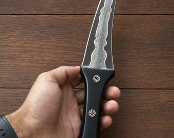 May include: A fixed-blade knife with a curved, pointed steel blade featuring a central Damascus pattern with copper accents. The handle is smooth, matte black with three circular gold-toned decorative inlays arranged vertically along the grip.
