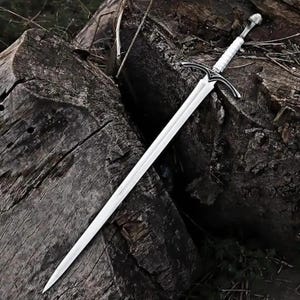 May include: A long, double-edged steel sword featuring a pointed tip, a central fuller running down the blade, and a crossguard with curved quillons. The handle is wrapped in white material and finished with a rounded, metallic pommel at the end.