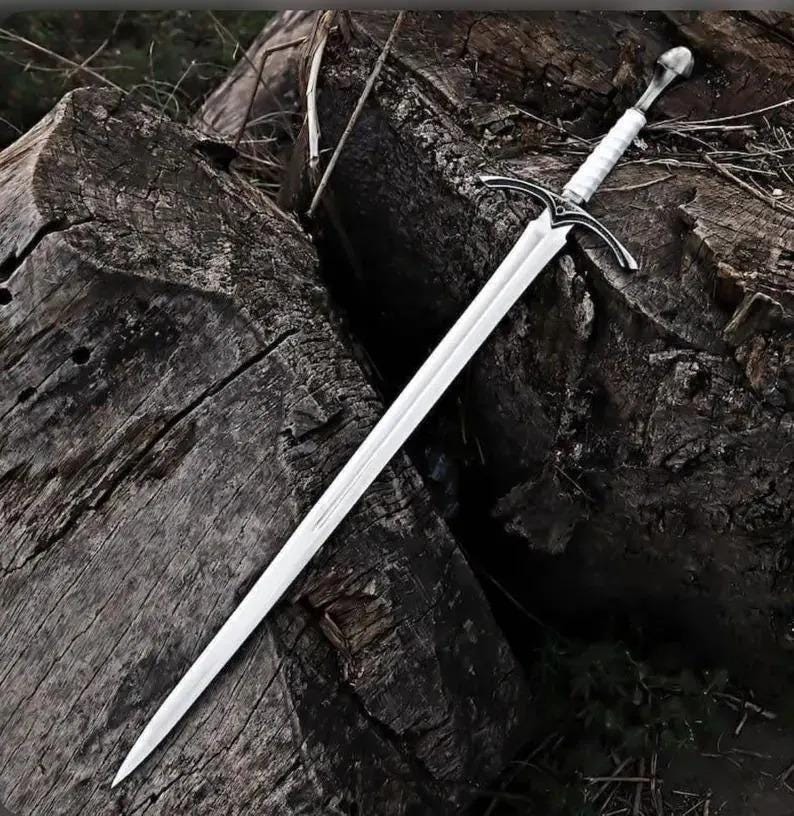 May include: A long, double-edged steel sword featuring a pointed tip, a central fuller running down the blade, and a crossguard with curved quillons. The handle is wrapped in white material and finished with a rounded, metallic pommel at the end.