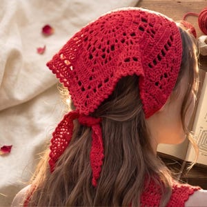 May include: A vibrant red crochet headscarf featuring an intricate openwork pattern and a triangular shape. The headscarf is tied at the back with two long, pointed ends. The design includes a central circular motif and a delicate scalloped edge.