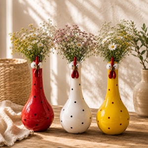 Puede incluir: Tres jarrones de cerámica con forma de gallina, cada uno con un cuello largo y una base redondeada. Los jarrones son rojos, blancos y amarillos, decorados con lunares negros. Cada gallina tiene ojos blancos, pico marrón y cresta roja.