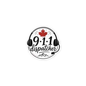 May include: A circular sticker featuring a black line drawing of headphones framing the text 9.1.1 dispatcher in black font. A red maple leaf is positioned above the numbers, and a black mountain range graphic is located below the text.