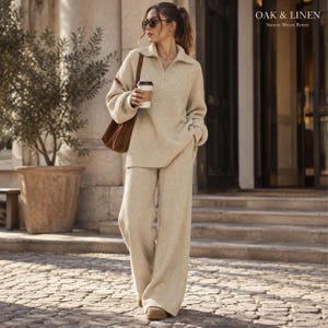 Op de afbeelding: Een beige tweedelige set van geribd breiwerk, bestaande uit een trui met lange mouwen en een kwartritssluiting en een bijpassende broek met wijde pijpen. De outfit is gecombineerd met een bruine schoudertas en beige schoenen. Tekst: OAK & LINEN Nature Wears Better.