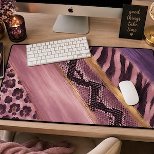 May include: A rectangular desk mat featuring a multi-panel design with a mauve leopard print, a solid mauve brushstroke section, a central black and mauve snakeskin pattern, a gold diagonal stripe, and a mauve and black zebra print section.