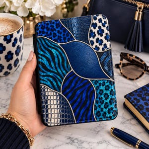 May include: A rectangular e-reader case featuring a patchwork design of blue and black patterns, including animal prints, textured scales, and smooth metallic sections separated by thin silver lines, creating a multi-textured appearance.