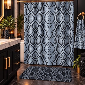 May include: A shower curtain, a matching hand towel, and a rectangular bath mat, all featuring a repeating black and light blue snakeskin pattern. The shower curtain hangs from a gold rod, while the towel is displayed on a gold ring holder.