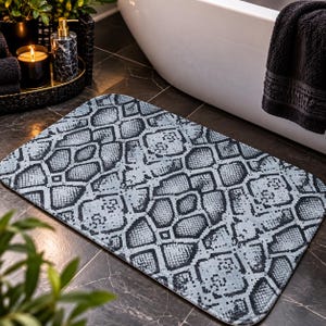May include: A rectangular bath mat featuring a repeating black and light gray snakeskin pattern. The mat has rounded corners and a soft, textured surface, displaying a detailed scale design that covers the entire top side of the floor covering.