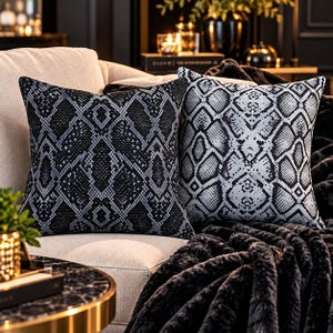 May include: Two square throw pillows featuring a high-contrast snakeskin pattern. One pillow displays a black and dark gray scale design, while the other features a light gray and black scale pattern. Both pillows have a textured, woven appearance.