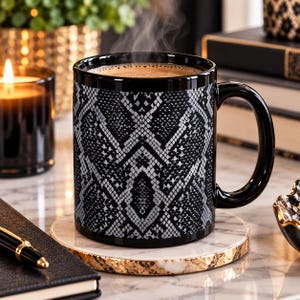 May include: A black ceramic mug featuring a grey and black snakeskin pattern. The mug has a glossy black handle and rim, and it is filled with a hot beverage that is emitting a small amount of steam from the top of the liquid surface.