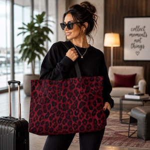 May include: A large rectangular tote bag featuring a bold red and black leopard print pattern. The bag has two black shoulder straps and a spacious main compartment, constructed from a soft fabric material with a consistent animal print design.