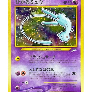 May include: A Japanese Shining Mew trading card featuring a holographic illustration of the light blue psychic-type creature. The card displays the name Hikaru Mew, HP 50, and includes detailed Japanese text, attack descriptions, and the number 151.