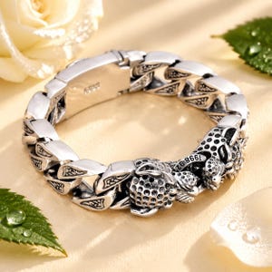 Puede incluir: Una pulsera de eslabones de plata con un motivo detallado de cabeza de leopardo con una superficie texturizada y moteada. Los eslabones de metal están grabados con patrones intrincados y el cierre tiene grabado el texto 925, indicando plata de ley.