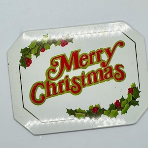 May include: White rectangular sign with a green holly leaf border and red berries. The sign says "Merry Christmas" in red and green letters.
