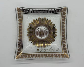 May include: A glass ashtray with a gold and purple design featuring a crown and the signature "Georges Briard".