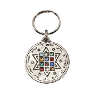 May include: A circular silver-toned metal keychain featuring a central Star of David design. The center contains a grid of twelve small, multi-colored faceted stones in various hues. Hebrew text is engraved along the outer circular border.