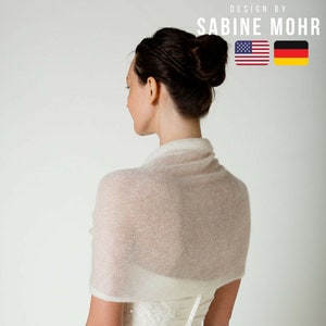May include: A white knitted shawl draped over a woman's shoulders. The shawl is made of a soft, delicate fabric and has a simple, elegant design. The woman is wearing a white dress and has her hair pulled back in a bun. The text "Luise" and "STRICKANLEITUNG" is visible at the bottom of the image.