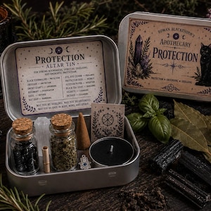 May include: A silver metal altar tin labeled Protection containing two small glass jars with cork stoppers, one filled with black stones and one with dried herbs, a small incense cone, a black tea light candle, a metal charm, and a paper card.
