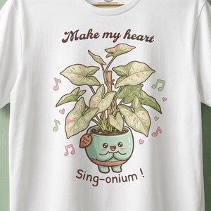 Peut inclure: Un t-shirt blanc avec une illustration d'une plante Syngonium en pot au visage souriant. Le texte au-dessus indique "Make my heart" et en dessous "Sing-onium!". La plante a des feuilles panachées vert et rose, entourée de notes de musique.