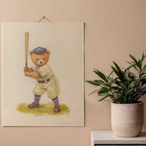 May include: A rectangular wall hanging featuring a watercolor illustration of a brown teddy bear dressed in a vintage baseball uniform, including a blue cap and cream-colored jersey, holding a wooden bat while standing on a patch of green grass.
