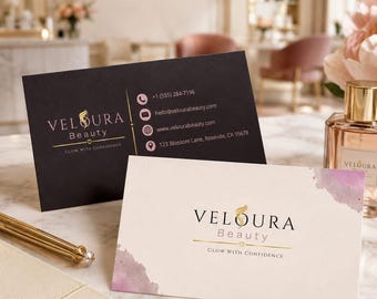 May include: Two rectangular business cards for Veloura Beauty. One card is black with gold text, including contact details and the slogan Glow With Confidence. The other card is cream-colored with a pink watercolor accent and the same gold logo.