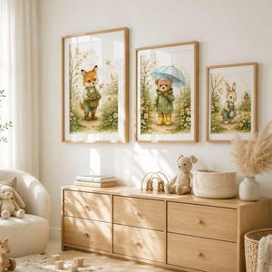 May include: Three framed wall art prints featuring watercolor illustrations of a fox holding a basket, a bear holding a blue umbrella, and a rabbit holding a watering can, all set in a garden scene with yellow flowers and light green foliage.
