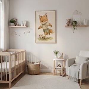 May include: A framed wall art print featuring a watercolor-style illustration of a fox wearing a light-colored shirt and green shorts, running while kicking a soccer ball on a grassy field. The artwork is displayed in a light wood frame.