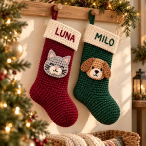 May include: Two crocheted Christmas stockings hanging from a wooden rack. The left stocking is deep red with a cream cuff embroidered with the name LUNA and a gray cat face. The right stocking is dark green with a cream cuff, the name MILO, and a dog face.