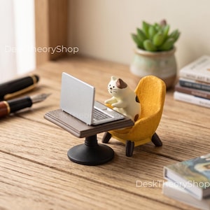 Könnte beinhalten: Eine Miniaturfigur einer cremefarbenen und braunen Katze, die in einem gelben Sessel an einem kleinen braunen Tisch mit einem silbernen Laptop sitzt. Der Text DeskTheoryShop ist in der oberen linken und unteren rechten Ecke zu sehen.