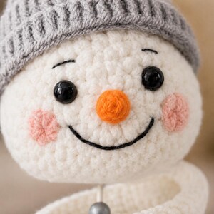 Close up of crocheted snowman face with orange nose and grey hat