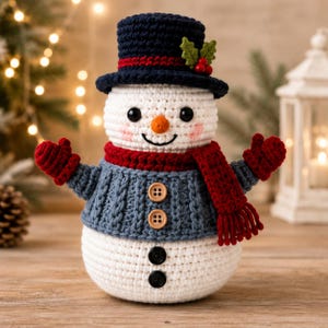 May include: A crocheted snowman figurine featuring a white body, a dark blue top hat with a holly sprig, a red scarf, and red mittens. The snowman wears a blue jumper with two light brown buttons and has two black buttons on its lower body.