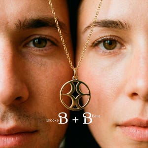 May include: A gold-toned circular pendant necklace featuring a cutout geometric design suspended on a delicate chain. The text Brooke B + B Bella is printed in white at the bottom center of the image, positioned between two faces.