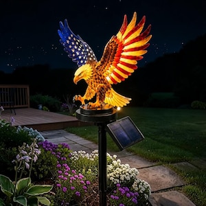 May include: A solar-powered garden stake featuring a sculpted eagle with wings spread wide. One wing displays a blue field with white stars, while the other wing and body feature red, white, and yellow tones. A black solar panel is attached to the pole.