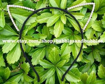 May include: Black headband with crystal frosted cat ears. The headband is on a bed of green leaves.