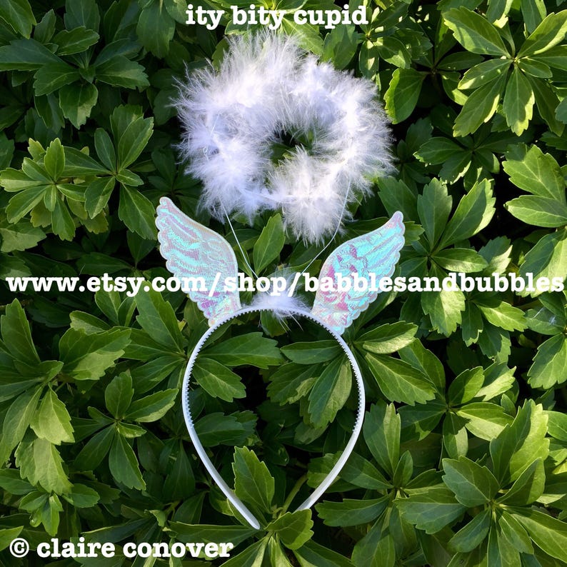 May include: A white headband with iridescent angel wings and a white halo with feathers. The headband is on a green leafy background. www.etsy.com/shop/babblesandbubbles