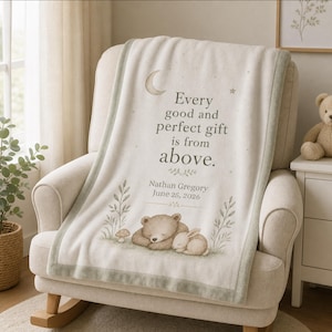 May include: A cream-colored fleece blanket with a sage green border featuring a sleeping bear and rabbit illustration, a crescent moon, and the text: Every good and perfect gift is from above. Nathan Gregory June 25, 2026, printed in dark gray.