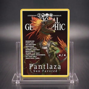 Puede incluir: Una carta coleccionable rectangular con la ilustración de un dinosaurio con plumas naranjas, armadura metálica y el texto National Geographic, Pantlaza Sun-Favored y reglas de juego. La carta está en un soporte de acrílico transparente.