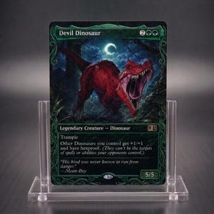 Könnte beinhalten: Eine Devil Dinosaur Sammelkarte mit einem roten Dinosaurier mit offenem Maul unter einer Mondsichel, präsentiert auf einem transparenten Acrylständer. Der Kartentext enthält Legendary Creature, Dinosaur, Trample sowie 5/5 Werte.