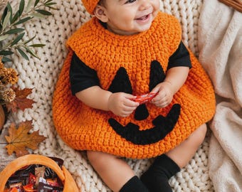 May include: A crochet pumpkin costume consisting of a bright orange sleeveless tunic with a black jack-o'-lantern face and a matching orange beanie with a green stem. The outfit is worn over a black short-sleeved shirt and black socks.