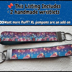 May include: Two fabric wristlets with a dark blue and purple gradient background featuring a floral pattern and cartoon teapot characters. Each wristlet has a dark metal hardware clasp and a circular key ring attached to one end of the strap.