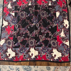 May include: A square scarf featuring a complex paisley pattern in shades of red, black, cream, and grey. The design includes a central black panel surrounded by floral motifs and geometric borders. The word OSCAR is printed in the bottom right corner.