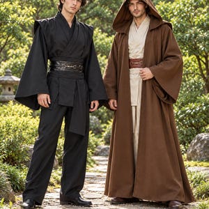 Peut inclure: Deux tenues composées de tuniques à manches longues et de pantalons larges. Un ensemble est noir uni avec une large ceinture en similicuir foncé. L'autre est beige avec une robe à capuche marron et une ceinture marron à boucle métallique.