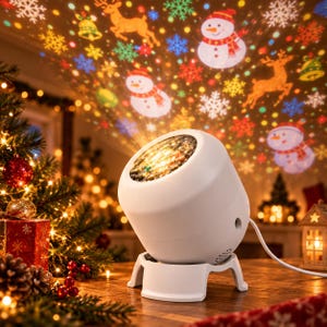 Può includere: Un proiettore di luci natalizie sferico bianco su un piccolo supporto proietta motivi luminosi colorati di pupazzi di neve, renne, campane e fiocchi di neve. Il dispositivo presenta una lente circolare e un cavo di alimentazione bianco.