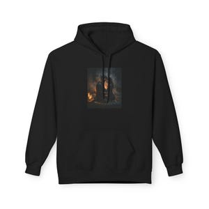 May include: A black hooded sweatshirt featuring a rectangular graphic print on the chest. The print depicts two figures sitting together in a dimly lit, atmospheric space illuminated by warm, glowing candles, creating a soft, hazy visual effect.